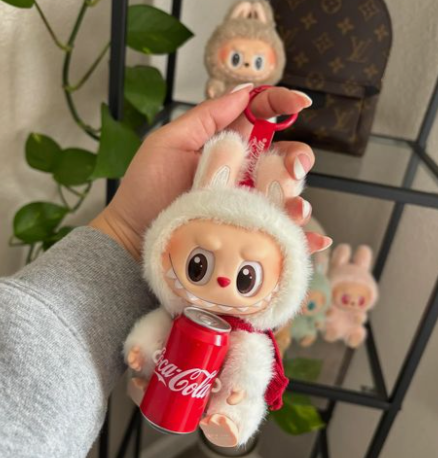 Coca cola limited edition white labubu wearing a red tie and a beige furry labubu in the background 