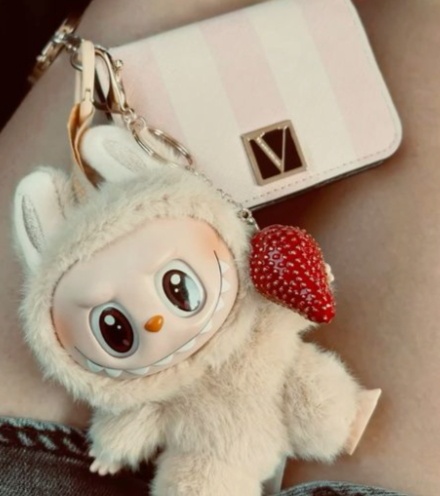 cute labubu doll in the lap of a girl wearing short denims where the collectible attached to her bag along with a strawberry