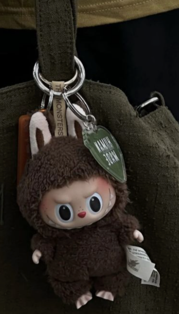 aesthetic brown labubu by popmart x the monsters hanging to an olive green purse that looks like a fashion statement 